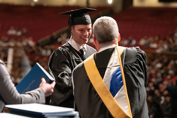 Graduates walk across the stage and accept their diploma.
