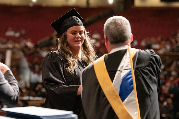 Graduates walk across the stage and accept their diploma.