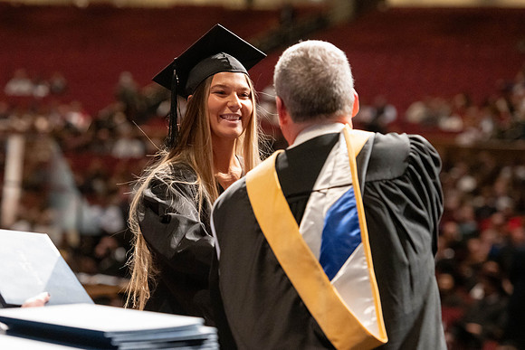 Graduates walk across the stage and accept their diploma.