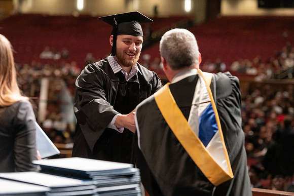 Graduates walk across the stage and accept their diploma.