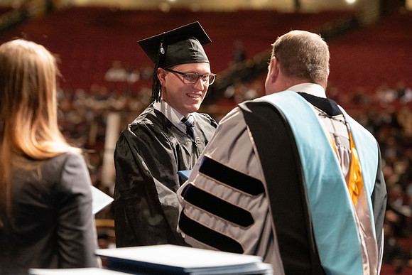 Graduates walk across the stage and accept their diploma.