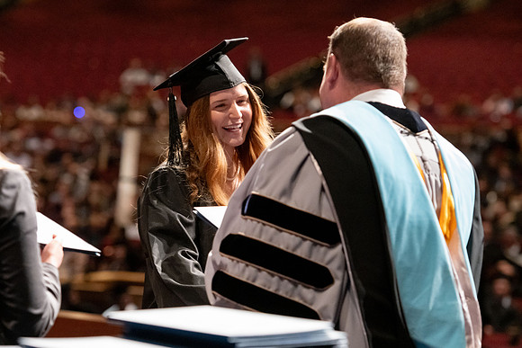 Graduates walk across the stage and accept their diploma.