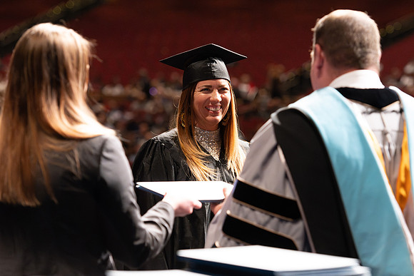 Graduates walk across the stage and accept their diploma.