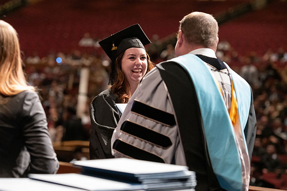 Graduates walk across the stage and accept their diploma.