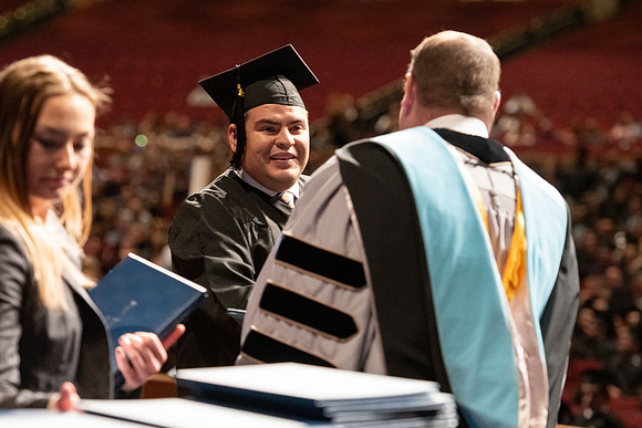 Graduates walk across the stage and accept their diploma.