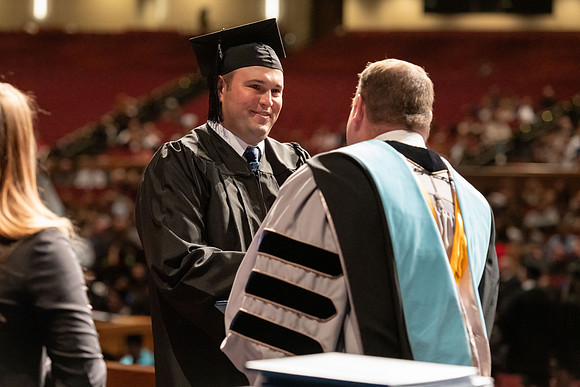 Graduates walk across the stage and accept their diploma.