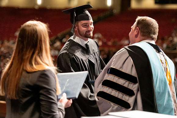 Graduates walk across the stage and accept their diploma.