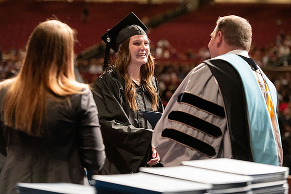 Graduates walk across the stage and accept their diploma.