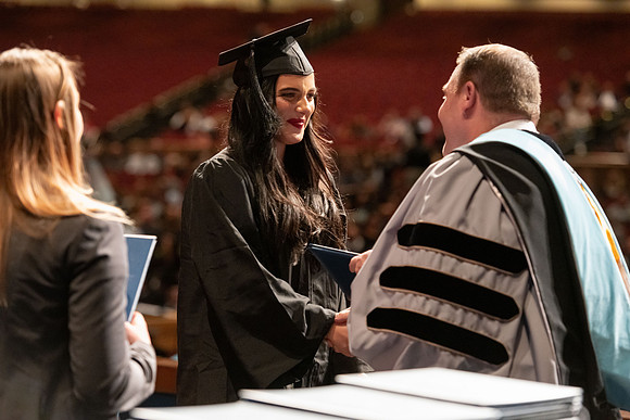 Graduates walk across the stage and accept their diploma.