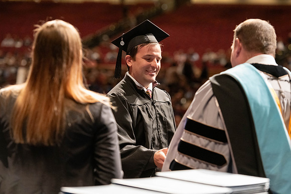 Graduates walk across the stage and accept their diploma.