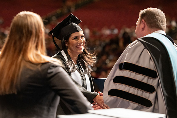 Graduates walk across the stage and accept their diploma.