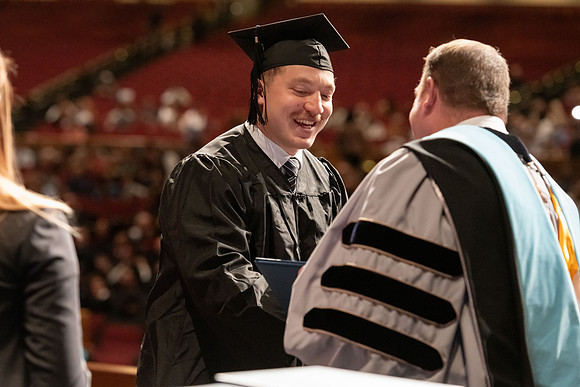 Graduates walk across the stage and accept their diploma.