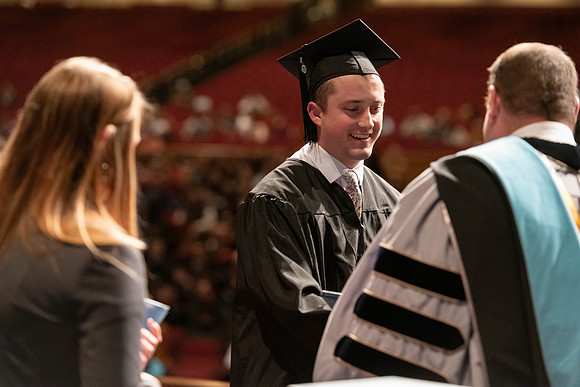 Graduates walk across the stage and accept their diploma.
