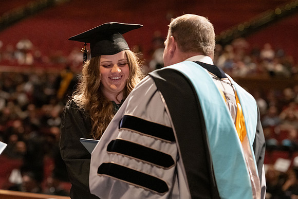 Graduates walk across the stage and accept their diploma.