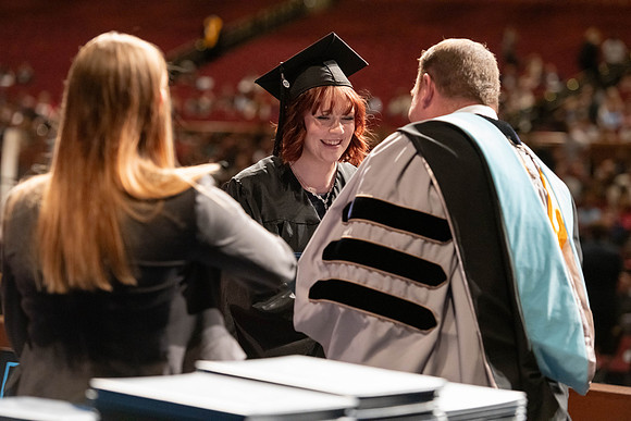 Graduates walk across the stage and accept their diploma.