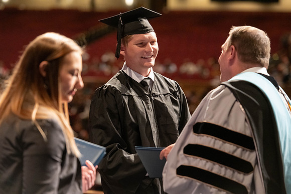 Graduates walk across the stage and accept their diploma.