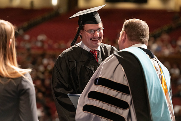 Graduates walk across the stage and accept their diploma.