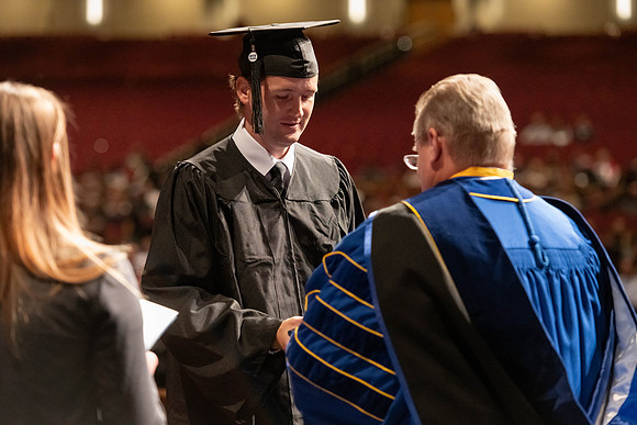 Graduates walk across the stage and accept their diploma.