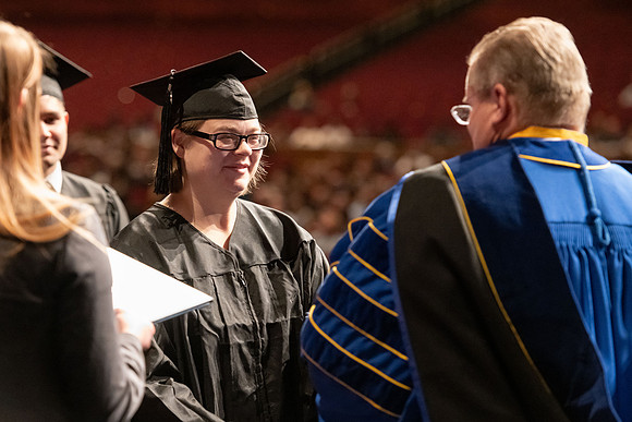 Graduates walk across the stage and accept their diploma.