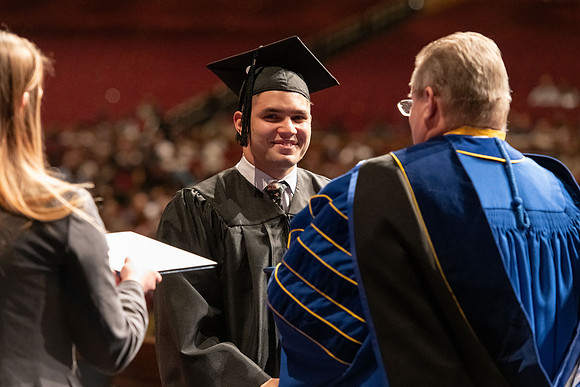 Graduates walk across the stage and accept their diploma.