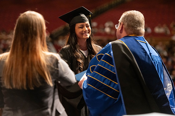 Graduates walk across the stage and accept their diploma.