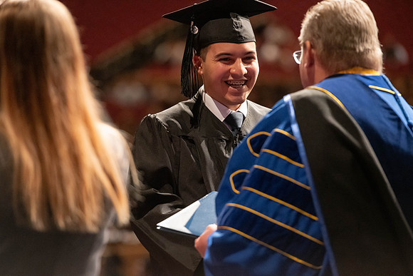 Graduates walk across the stage and accept their diploma.