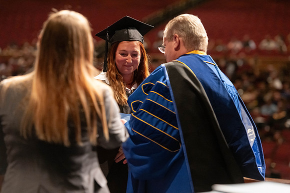 Graduates walk across the stage and accept their diploma.