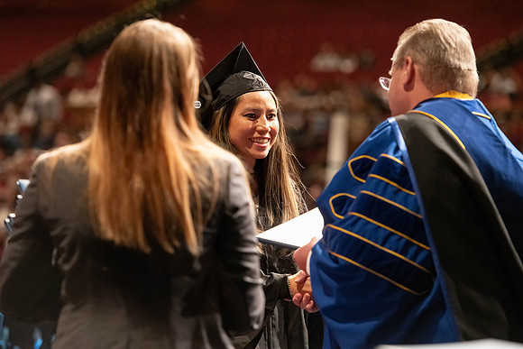 Graduates walk across the stage and accept their diploma.