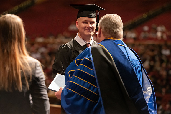 Graduates walk across the stage and accept their diploma.