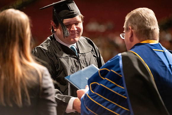 Graduates walk across the stage and accept their diploma.