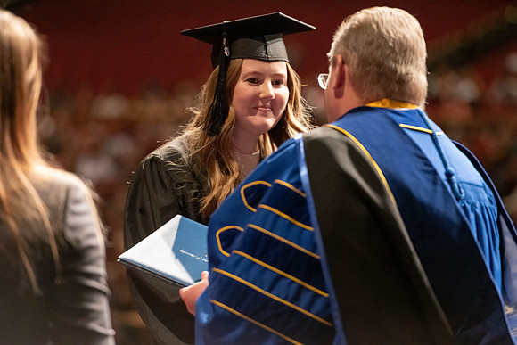 Graduates walk across the stage and accept their diploma.