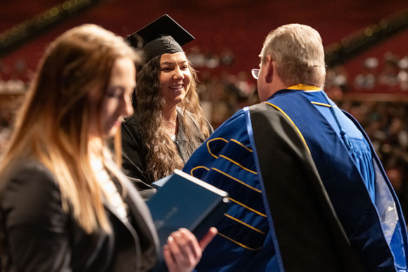 Graduates walk across the stage and accept their diploma.