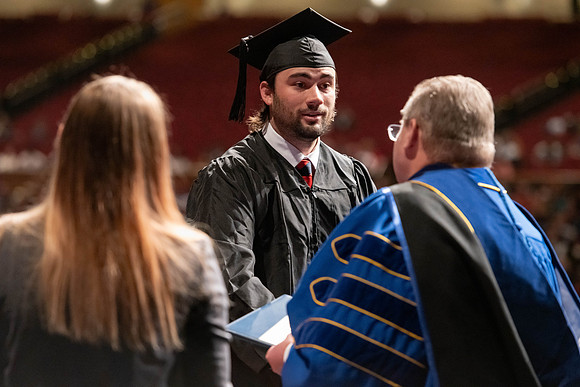 Graduates walk across the stage and accept their diploma.