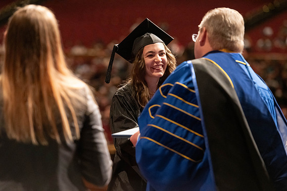 Graduates walk across the stage and accept their diploma.