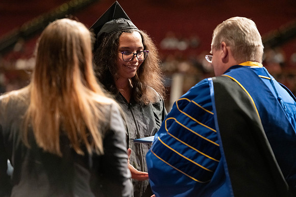 Graduates walk across the stage and accept their diploma.