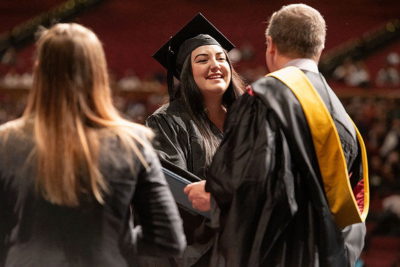 Graduates walk across the stage and accept their diploma.