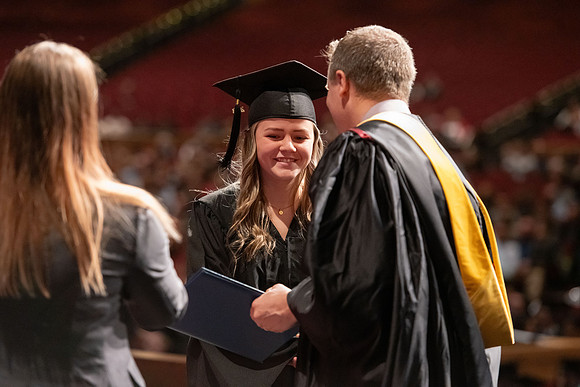 Graduates walk across the stage and accept their diploma.