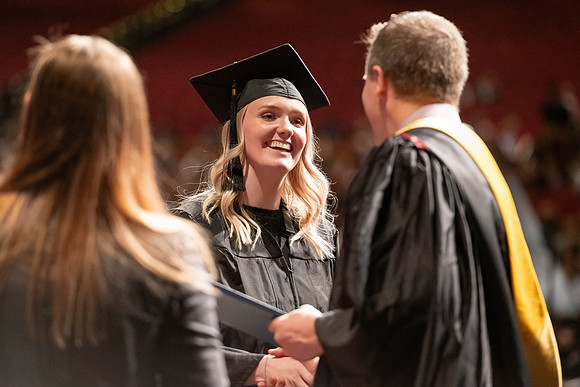 Graduates walk across the stage and accept their diploma.