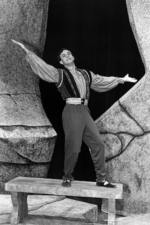 Actor standing on a stone bench with his arms extended.