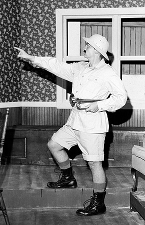 Scout with a trumpet in his left hand and pointing at something with his right hand.