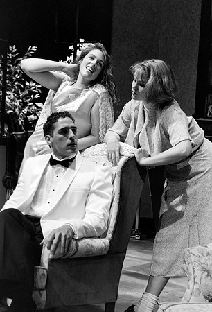 Two young actresses leaning over the chair while talking to a man.