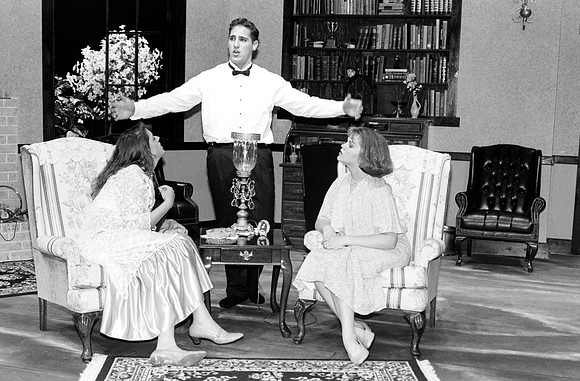the Man is extending his arms and talking, while the two ladies look at him.