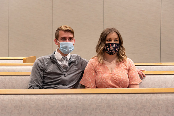 A couple of students sitting in a church pew, wearing face masks, waiting for church to start.
