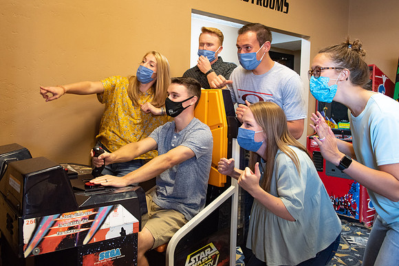 Students at a local movie theater wearing face masks, playing video games.