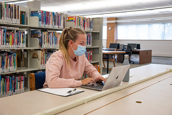 A student wearing a face mask studying in the library.