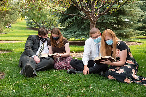 Students reading scriptures on the temple grounds while wearing face masks.