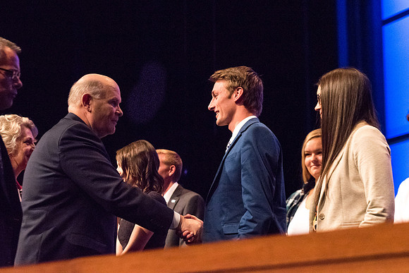 Elder Renlund shakes the hands of and greets those who sit on the stand at the end of his devotional address. 2017