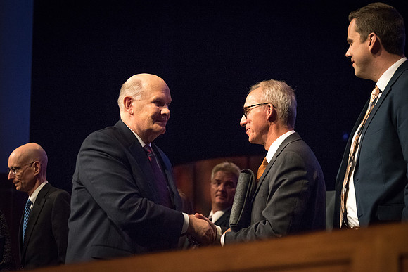 Elder Renlund shakes the hands of and greets those who sit on the stand at the end of his devotional address. 2017