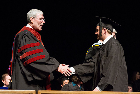 Edwin A. Sexton shakes hands with a graduate from the College of Business and Communication in the Hart Auditorium during Convocation.