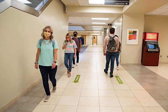 Examples of students staying safe and healthy during the COVID-19 pandemic by social distancing, following pathway arrows, and wearing face masks.